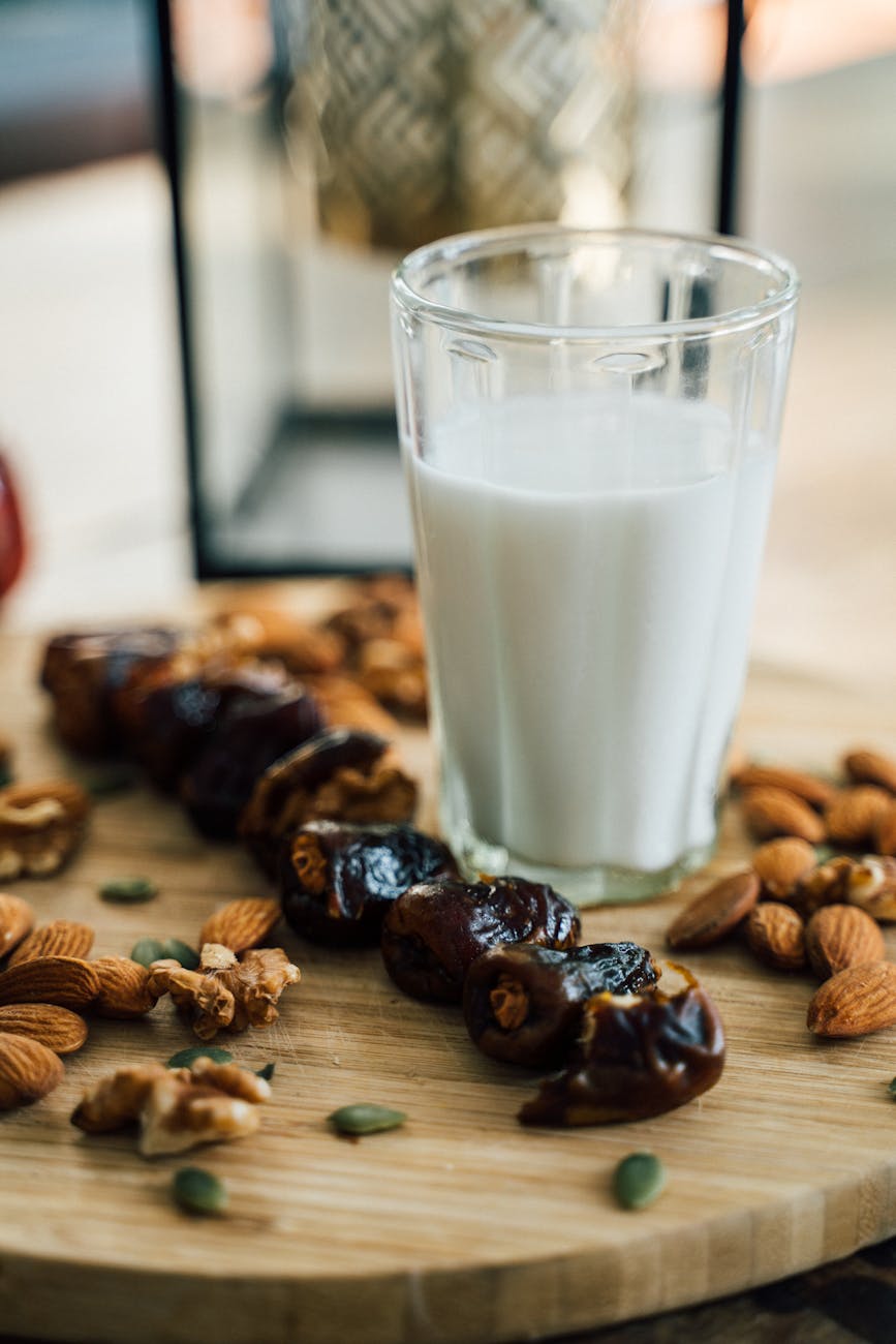 a glass of milk on a wooden board with dates and almonds
